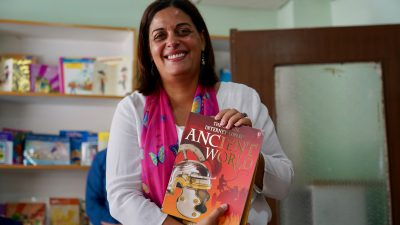 Saviour's School teacher smiles and poses with Ancient World textbook