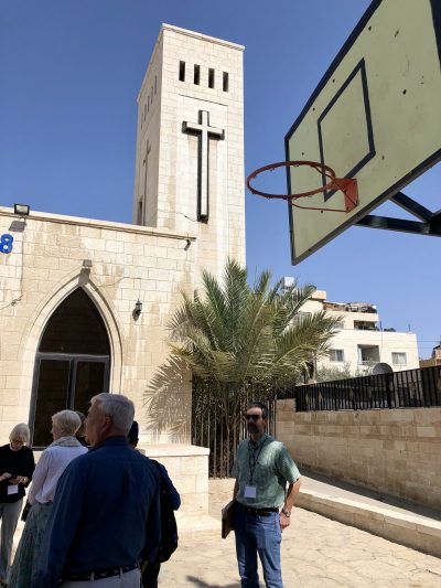 A photo of AFEDJ Trustees standing under a basketball hoop outside at St. Saviour's School in Zarqua.