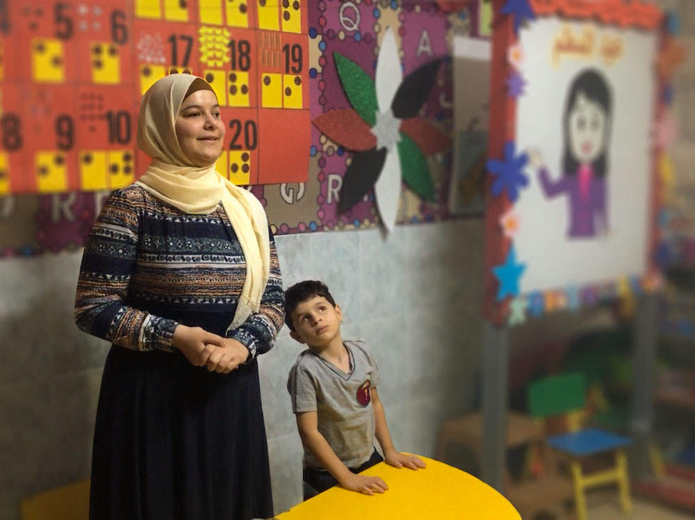 A young blind Muslim woman smiles as she stands in front of the classroom.