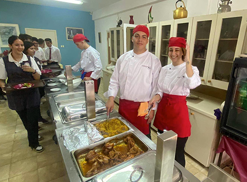 Two young chefs in red hats smile in front of the buffet line