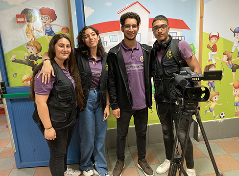 Teenagers stand in front of a mural posing with video camera equipment